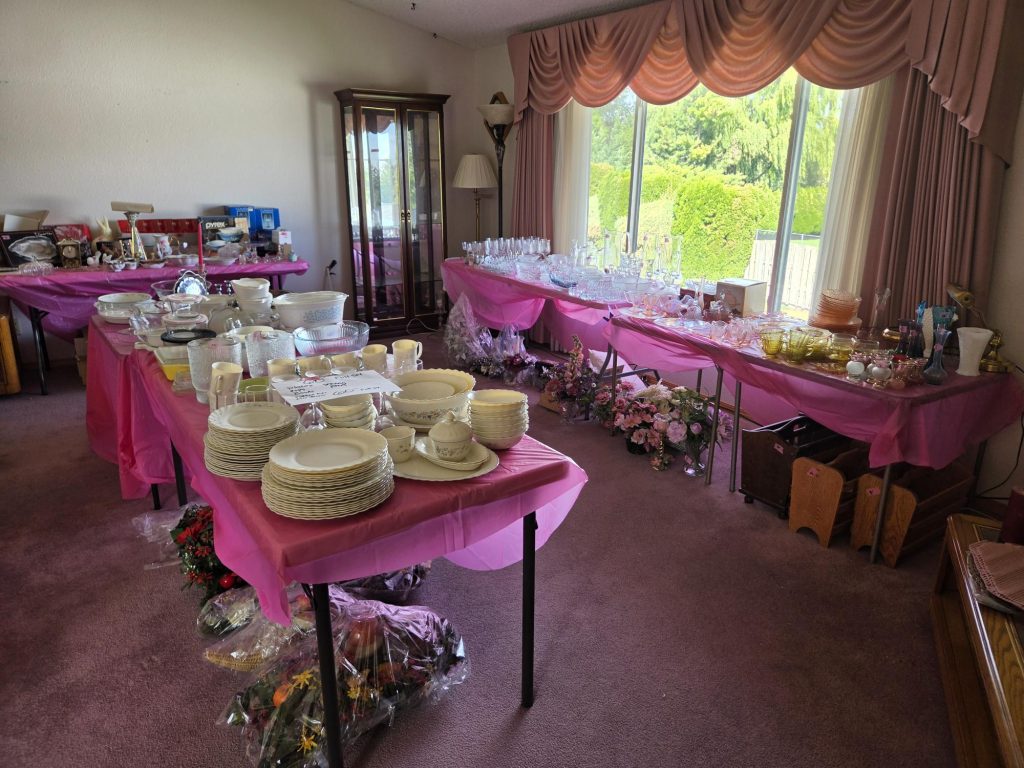 Estate sale in Tri-Cities, WA with dishware set out on pink-covered tables in a dining room